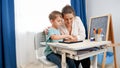 Young mother hugging her little son doing homework and studying on tablet computer at home. CHild using gadget for Royalty Free Stock Photo