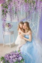 Young mother hugs her little daughter in a studio decorated a lilac flowers