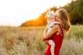 Young mother hugs little daughter in her arms at sunset in the field