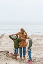 young mother and kids spending time together on seashore on cold