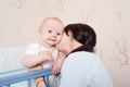 Young mother kissing baby boy, hugging in a cot. Royalty Free Stock Photo