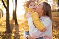 Young mother kissing her baby son in autumn park. Family on autumn walk in nature outdoors. Royalty Free Stock Photo