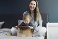 Young mother laughing at baby getting into cardboard package box. Toys received from online shop. Trusted delivery