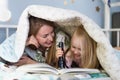 Mother laughing with happy daughter while reading a book under blanket using flashlight Royalty Free Stock Photo