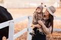 Young mother and little baby girl near a horses in autumn sunny day. Mother stroking a horse and smiling. mother`s day Royalty Free Stock Photo