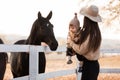 Young mother and little baby girl near a horses in autumn sunny day. Mother stroking a horse and smiling. mother`s day Royalty Free Stock Photo