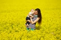 Young mother with little baby in hands in bright yellow field of flowers in sunny summer day, family love and sincerity