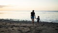 Young mother and little child are walking on the sandy beach and admire the sunset Royalty Free Stock Photo