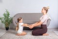 Young mother and little daughter keeping eyes closed sitting on floor, holding hands together and practicing yoga at home Royalty Free Stock Photo