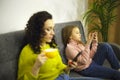 Young mother and little girl daughter using mobile phones while sitting separately on sofa at home Royalty Free Stock Photo