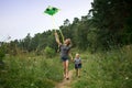 A young mother and a little girl are running along the path with a kite. Summer day, wildflowers Royalty Free Stock Photo