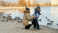 Young mother with little son feeding ducks with bread and seeds on lake in city park Royalty Free Stock Photo