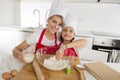 Young mother and little sweet daughter in cook hat and apron cooking together baking at home kitchen Royalty Free Stock Photo