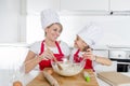 Young mother and little sweet daughter in cook hat and apron cooking together baking at home kitchen Royalty Free Stock Photo