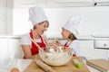 Young mother and little sweet daughter in cook hat and apron cooking together baking at home kitchen Royalty Free Stock Photo