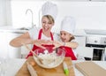 Young mother and little sweet daughter in cook hat and apron cooking together baking at home kitchen Royalty Free Stock Photo