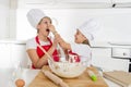 Young mother and little sweet daughter in cook hat and apron cooking together baking at home kitchen Royalty Free Stock Photo