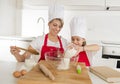 Young mother and little sweet daughter in cook hat and apron cooking together baking at home kitchen Royalty Free Stock Photo