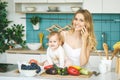 Young mother looking at camera and smiling, cooking and playing with her baby daughter in a modern kitchen. Using phone. Healthy Royalty Free Stock Photo