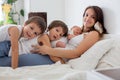 Young mother lying in bed with her newborn baby boy and his older brothers