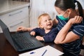 Young mother on maternity leave trying to freelance by the desk with toddler child. Royalty Free Stock Photo