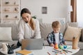 Young mother multitasking, talking on cellphone, using laptop and taking care of kid son, busy mom working online Royalty Free Stock Photo