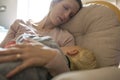 Young mother napping in a rocking chair with baby sleeping in h