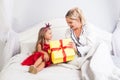 Young mother opening gift box with surprised amazed face, sitting with cute little daughter on bed, child wishing woman happy