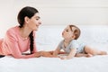 Young mother playing with her cute baby, talking and spending time together, lying on bed in bedroom at home Royalty Free Stock Photo