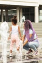 Young mother plays with a girl in the spray of a fountain in the park, summer, fun, heat Royalty Free Stock Photo