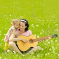 Young mother plays the guitar for her little daughter on green meadow Royalty Free Stock Photo