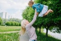 A young mother plays with her little daughter in the park, hold on to her hands. Throw the girl in the air