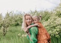 a young mother plays with her little daughter rolling her on her back in the middle of a green spring garden.