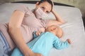 Young mother in protective face mask with newborn cute infant baby breastfeeds him with breast milk Royalty Free Stock Photo
