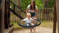 Young mother pushing her baby son swinging in rope nest swing in park. Kids playing outdoors, children having fun, summer vacation Royalty Free Stock Photo