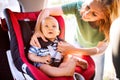 Young mother putting baby boy in the car seat. Royalty Free Stock Photo