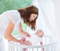 Young mother putting her newborn baby into crib