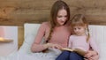 Young mother reading goodnight story book fairytale to child daughter kid girl in night bedroom Royalty Free Stock Photo