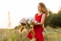 young mother in a red dress is circling in her arms a little daughter at sunset in the field