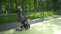 A young mother rides a gyro scooter and carries a stroller with a baby. Modern walk with a child in the park. Girl with
