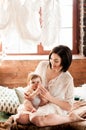 Young mother sits on the bed with her little daughter opposite the window Royalty Free Stock Photo