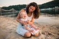 Young mother sitting on the beach with one year old baby son. Boy hugging, smiling, laughing, summer day. Happy childhood carefree Royalty Free Stock Photo