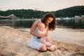 Young mother sitting on the beach with one year old baby son. Boy hugging, smiling, laughing, summer day. Happy childhood carefree Royalty Free Stock Photo