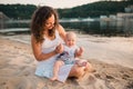 Young mother sitting on the beach with one year old baby son. Boy hugging, smiling, laughing, summer day. Happy childhood carefree Royalty Free Stock Photo