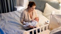 Young mother sitting next to baby crib with her newborn child at night in bedroom Royalty Free Stock Photo