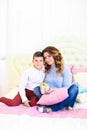 Young mother sitting with son and gift on bed. Royalty Free Stock Photo