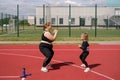 Young mother and skinny daughter play sports together, doing squat exercises on sports field. Plump woman with merrily laughing ch
