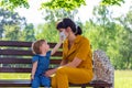 A young mother with a small baby daughter in a summer Park, a girl tries to take off the medical mask from her mother, the concep