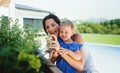 Young mother with small daughter outdoors in backyard garden, spraying plants.