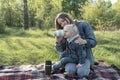 Young mother and small daughter on picnic. Girl drinks from cup. Green park on sunny spring day. Little girl sits on her mother`s